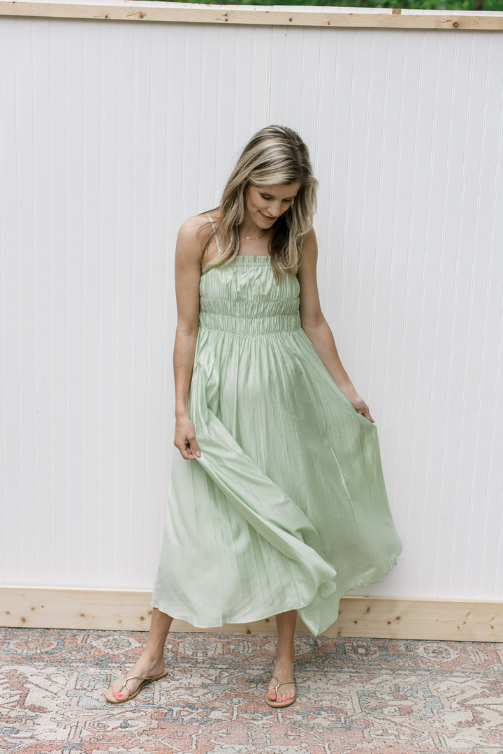 Model wearing sandals with a pale green midi with a smocked bust with adjustable straps.
