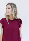 Close up of ruffle at round neck and cap sleeve on a wine above the knee dress. 