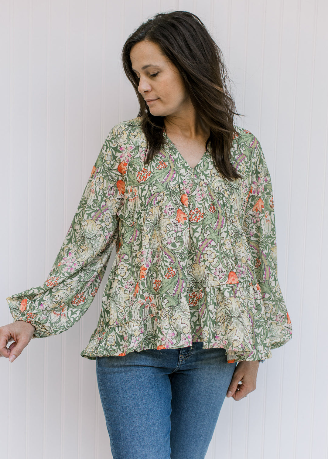 Model wearing a cream v-neck top with olive, coral and gold floral and bubble long sleeves. 