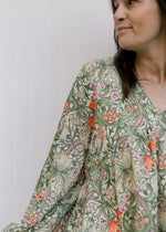 Close up of olive, coral and gold floral design on a cream top with a v-neck and bubble long sleeves