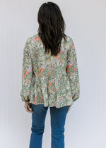 Back view of Model wearing a cream top with olive, coral and gold floral and bubble long sleeves.