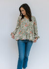 Model wearing jeans with a cream top with olive, coral and gold floral and bubble long sleeves. 