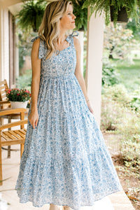 Model wearing wedges and a white midi with light blue floral, tie spaghetti straps and a v-neck. 