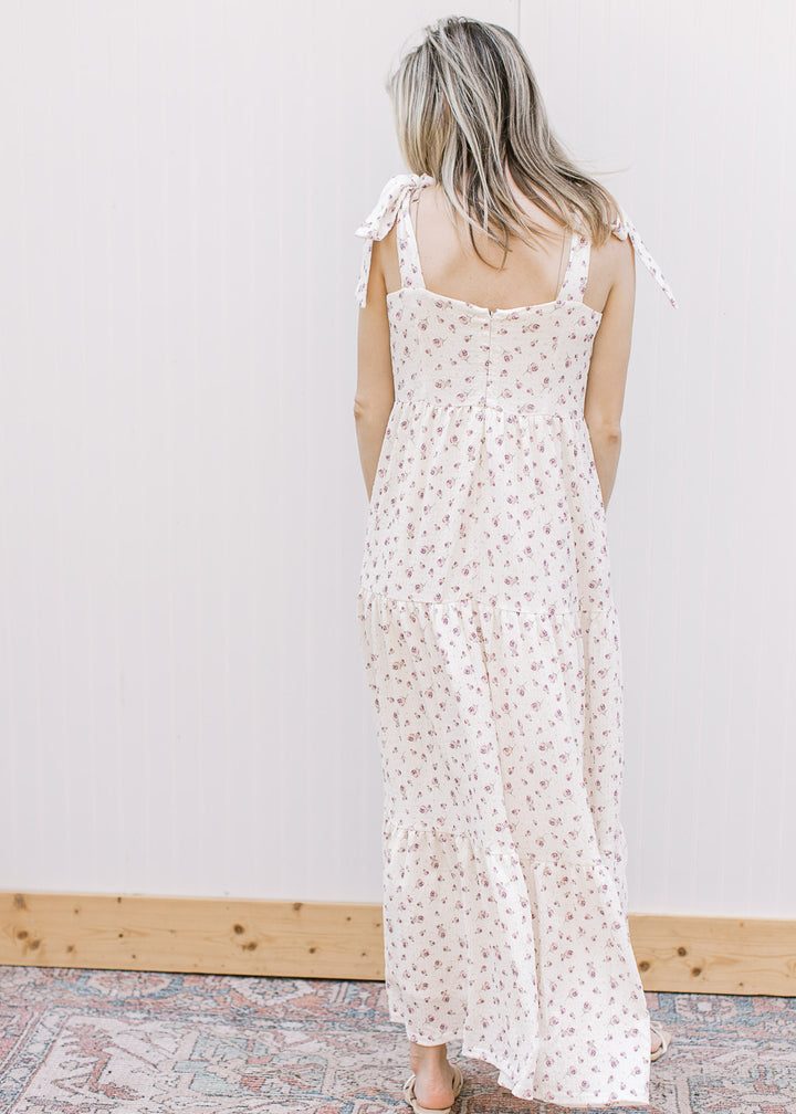 Back view of model wearing a cream midi with purple floral, v-neck, tie straps and tiered skirt.