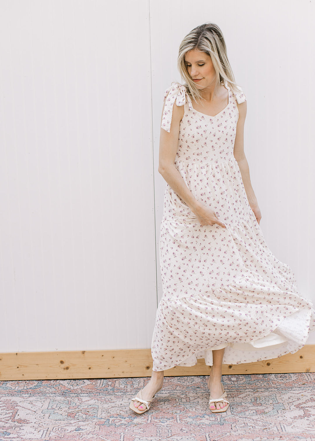 Model wearing heels and a cream midi with pale purple floral, v-neck, tie straps and tiered skirt.