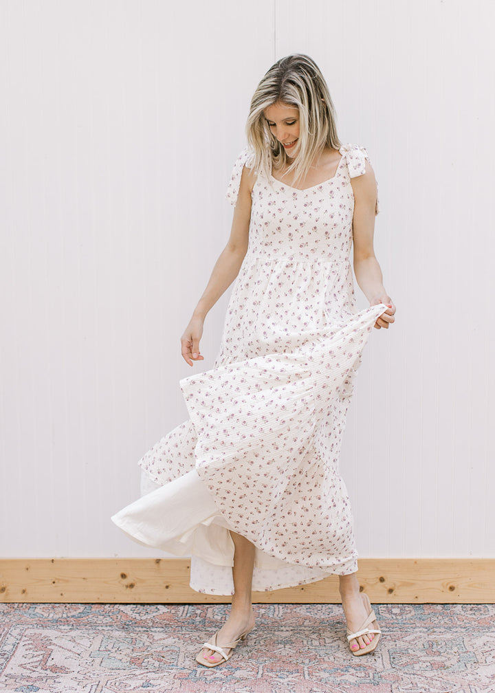 Model twirling in a cream midi with purple floral, v-neck, adjustable tie straps and tiered skirt. 