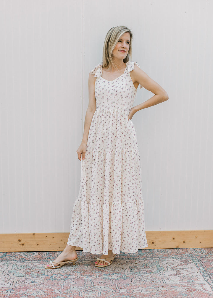 Model wearing a flowy cream midi with purple floral, v-neck, adjustable tie straps and tiered skirt.