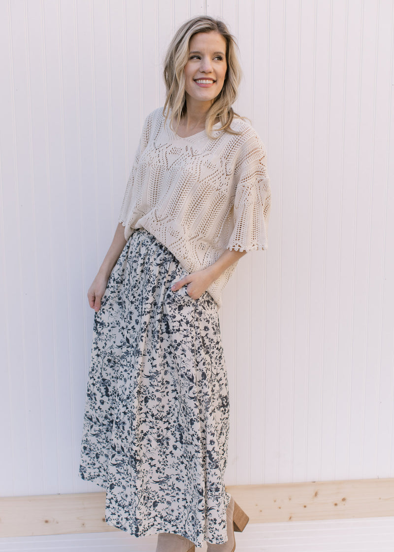 Model wearing a cream midi skirt with black floral pattern, pockets and an elastic waistband.