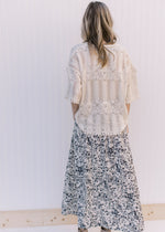 Back view of Model wearing a cream skirt with black floral pattern, pockets and an elastic waist.
