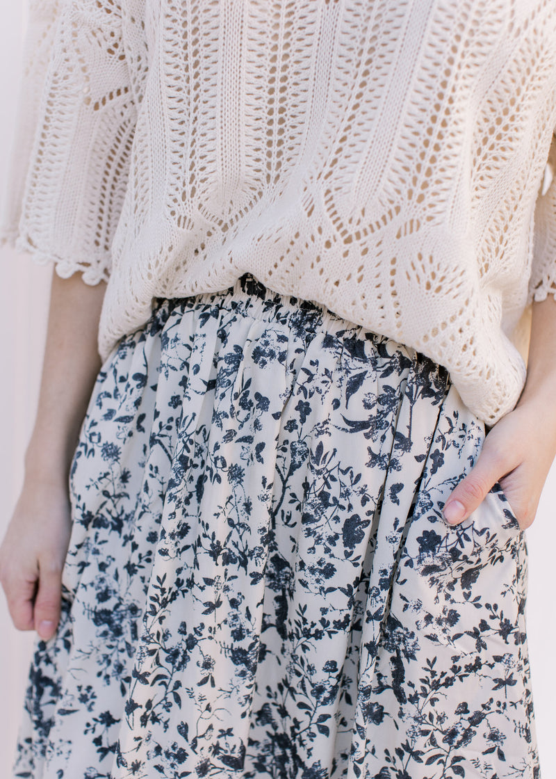 Model wearing a cream sweater with a cream skirt with black floral pattern and an elastic waist.