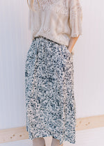 Model wearing a cream top, booties and a midi skirt with black floral pattern and an elastic waist.