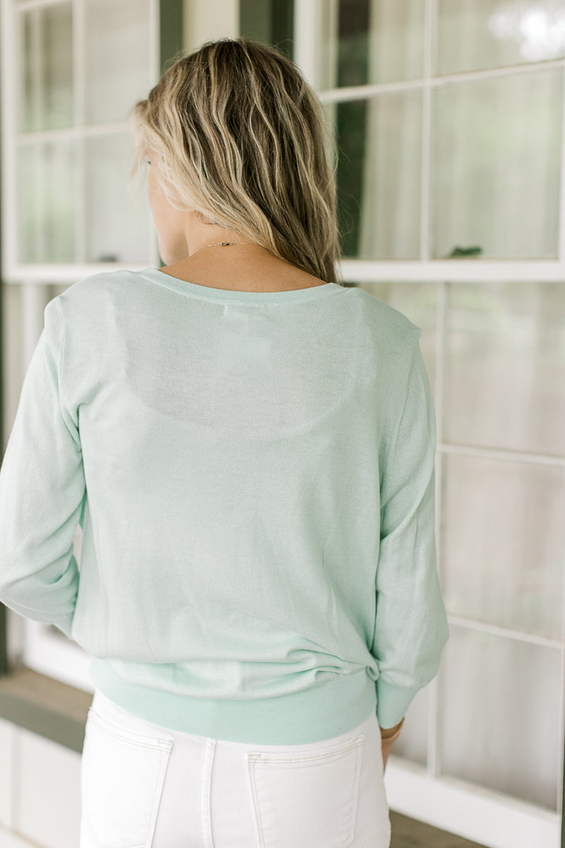 Back view of Model wearing a button up mint green cardigan with 3/4 sleeves.