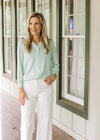 Model wearing white pants with a button up mint green cardigan with 3/4 sleeves.