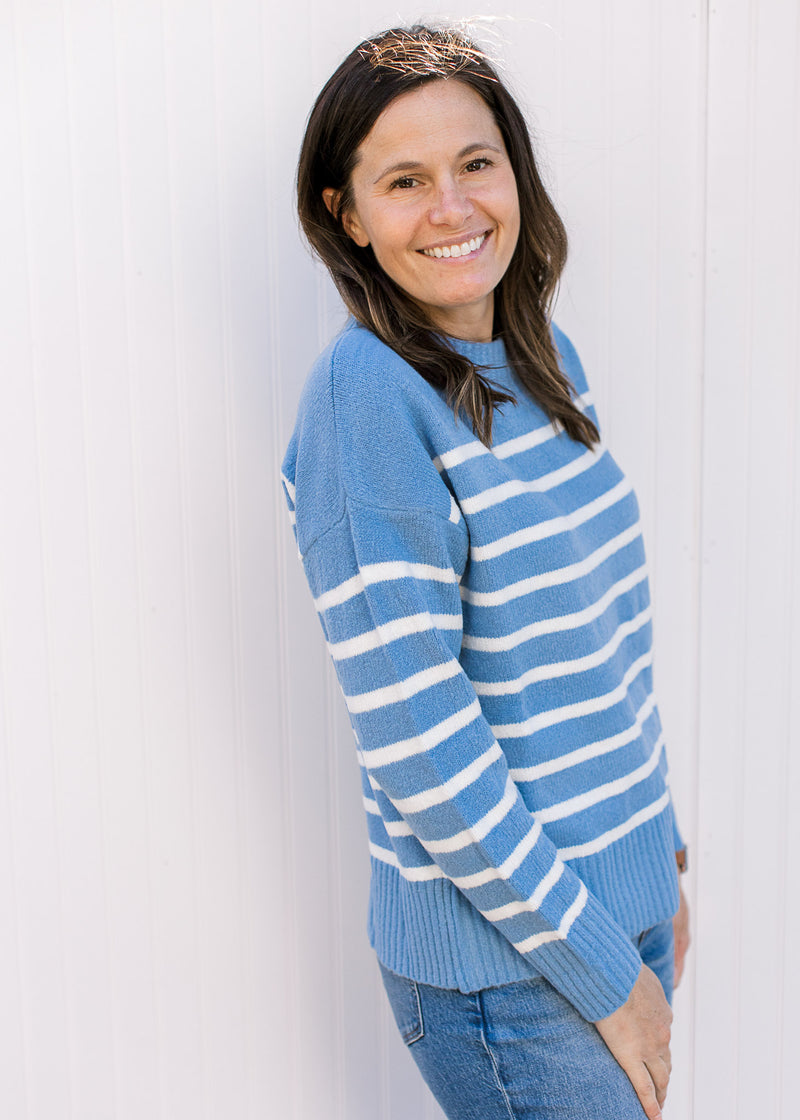 Side view of Model wearing a light blue long sleeve sweater with cream stripes and a round neck. 