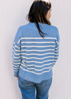Back view of a light blue sweater with cream stripes, long sleeves and a round neck. 