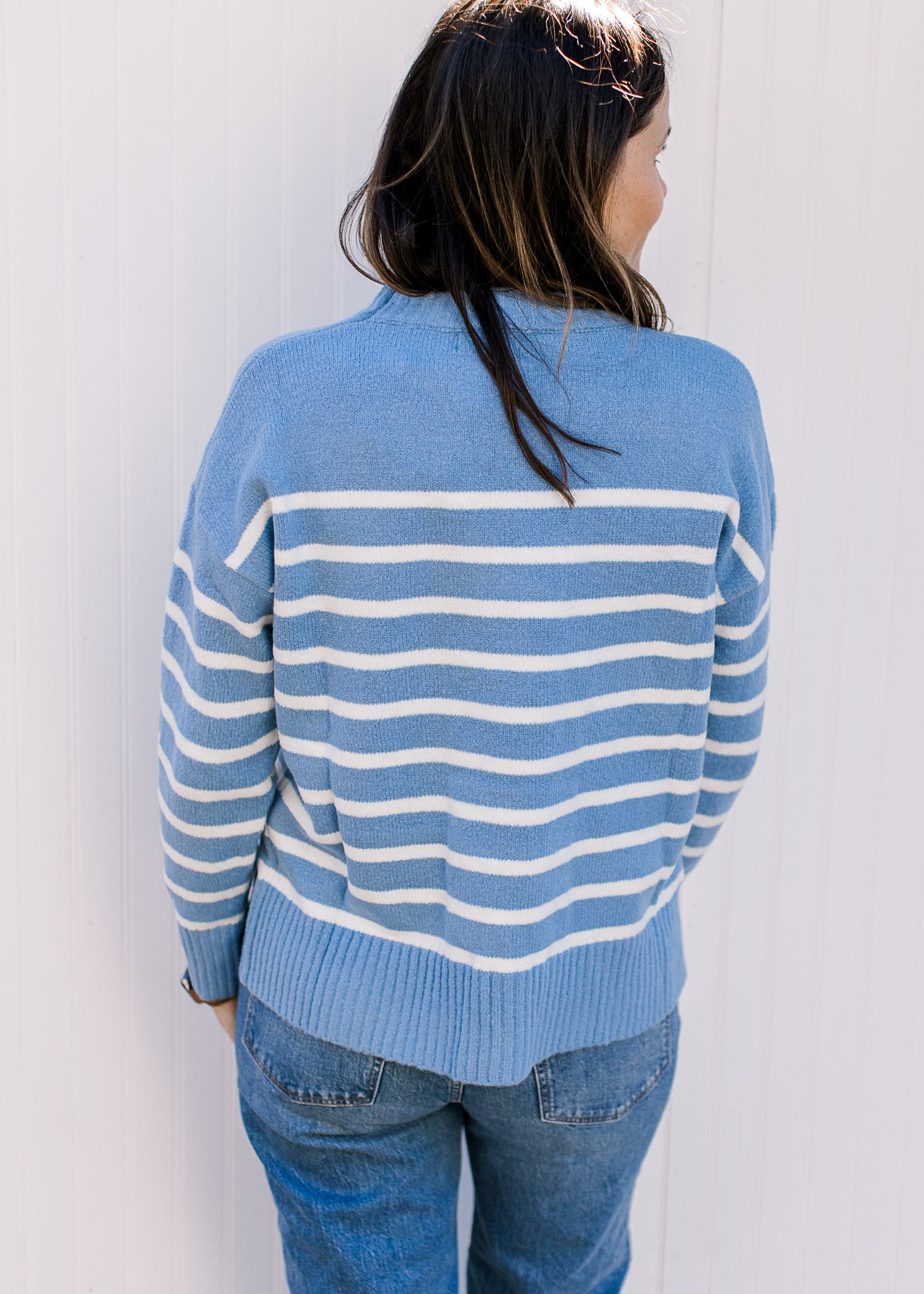 Back view of a light blue sweater with cream stripes, long sleeves and a round neck. 