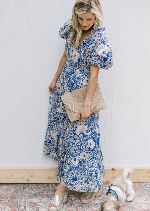 Model wearing a blue maxi dress with cream floral, ruffle neck and short puff sleeves.
