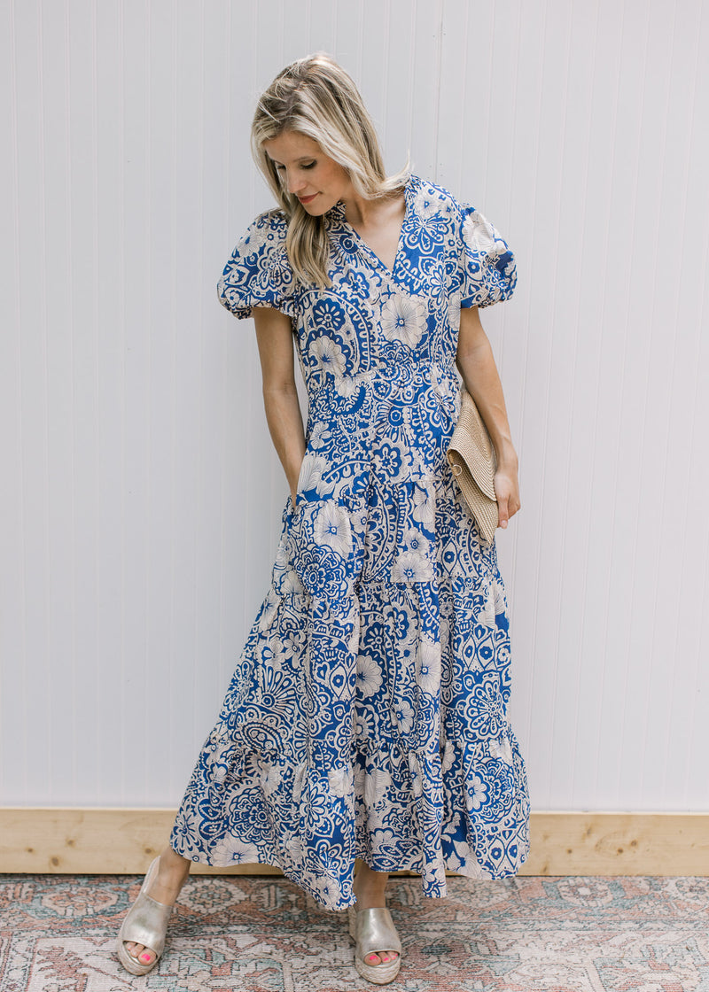 Model wearing sandals with a blue maxi dress with cream floral, ruffle neck and short puff sleeves.