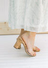 Side view of a model wearing heels with a clear vamp and a cork heel. 