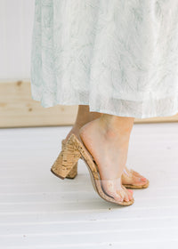 Side view of a model wearing heels with a clear vamp and a cork heel. 