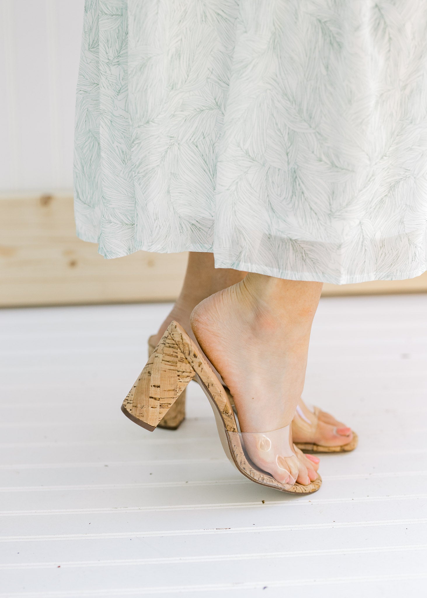 Side view of a model wearing heels with a clear vamp and a cork heel. 