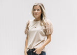 Model wearing a taupe top with short sleeves with a flocked dotted Swiss and a crew neck. 