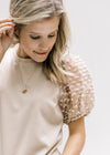 Model wearing a taupe top with bubble short sleeves with a flocked dotted Swiss and a crew neck. 
