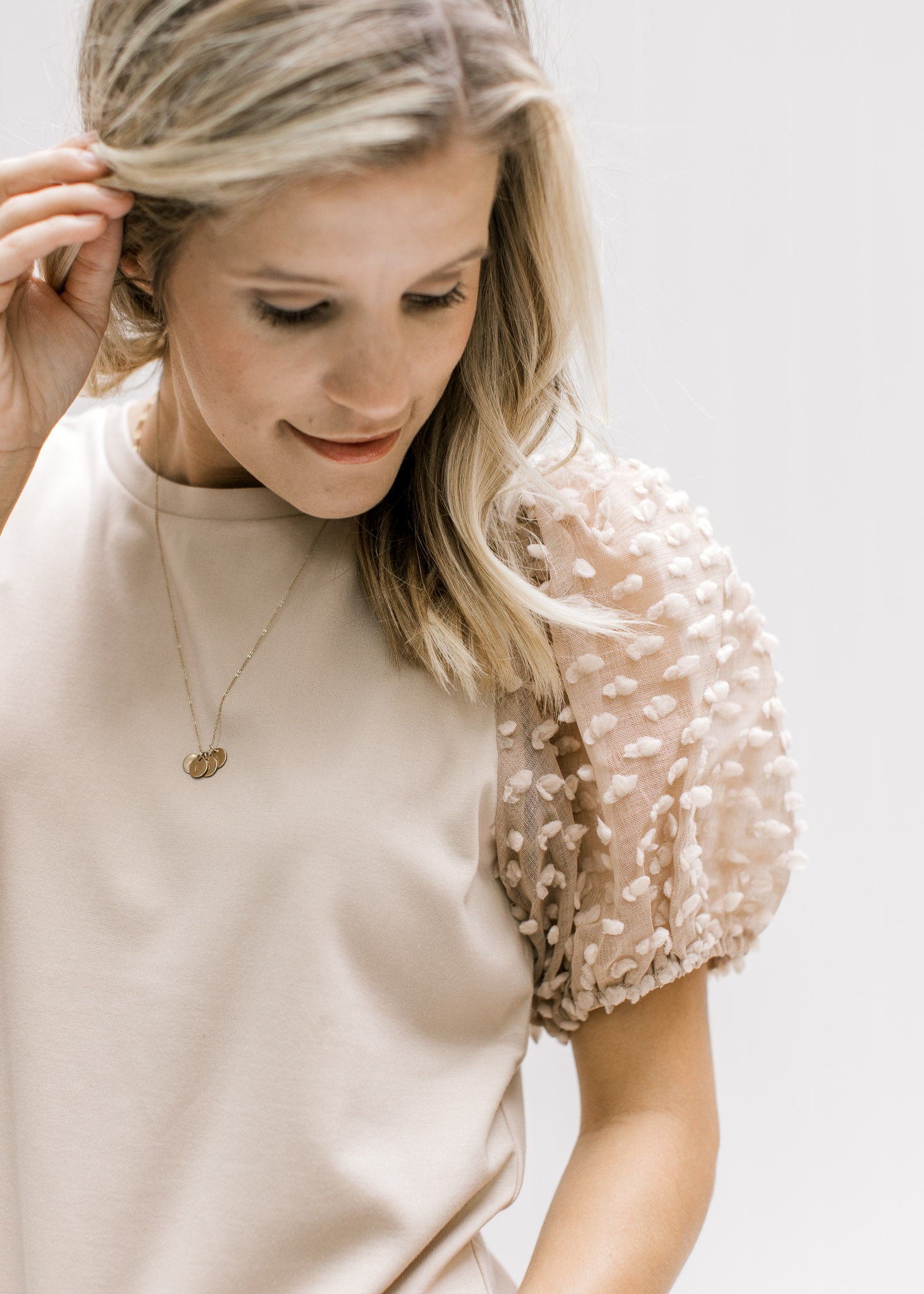 Model wearing a taupe top with bubble short sleeves with a flocked dotted Swiss and a crew neck. 