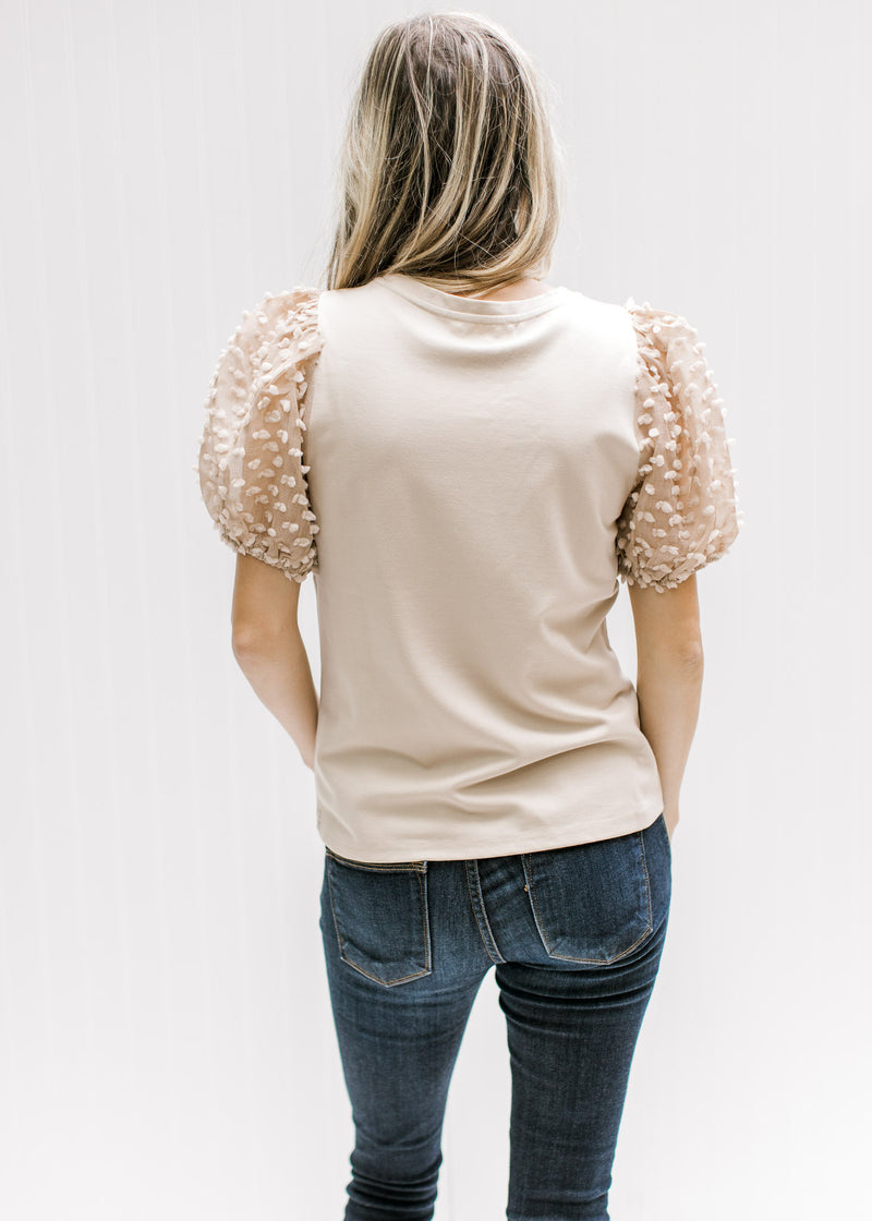 Back view of Model wearing a taupe top with short sleeves with a dotted Swiss and a crew neck. 