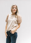 Model wearing jeans and a taupe top with bubble short sleeves and a flocked dotted Swiss. 
