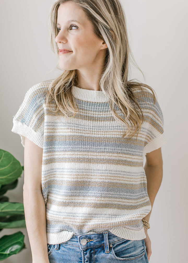 Model wearing a cream sweater with taupe and blue stripes, short sleeves and ribbed detail.