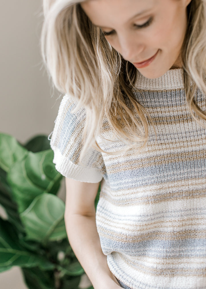 Close up of short sleeves and ribbing on a cream sweater with taupe and blue stripes. 