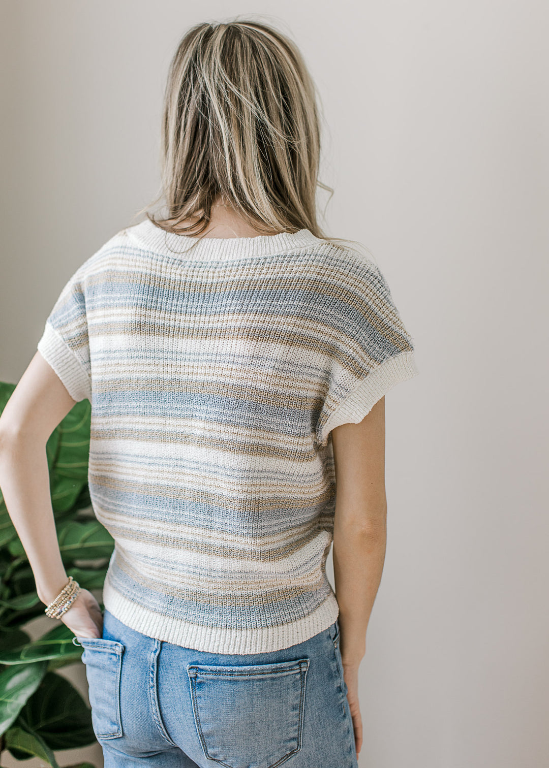Back view of Model wearing a cream sweater with taupe and blue stripes and short sleeves. 