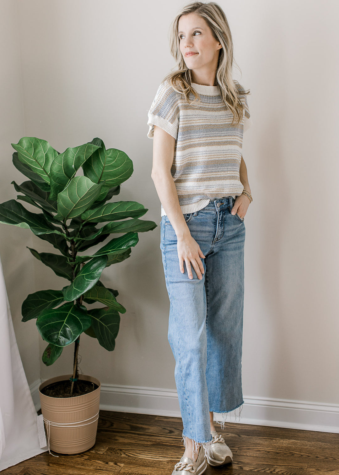 Model wearing jeans, slip ons and a cream sweater with taupe and blue stripes and short sleeves. 