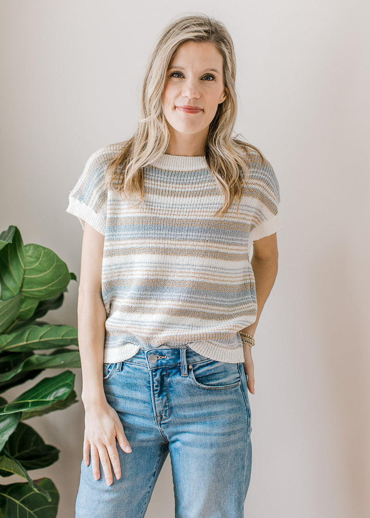 Model wearing jeans and a cream sweater with taupe and blue stripes, short sleeve and ribbed detail.
