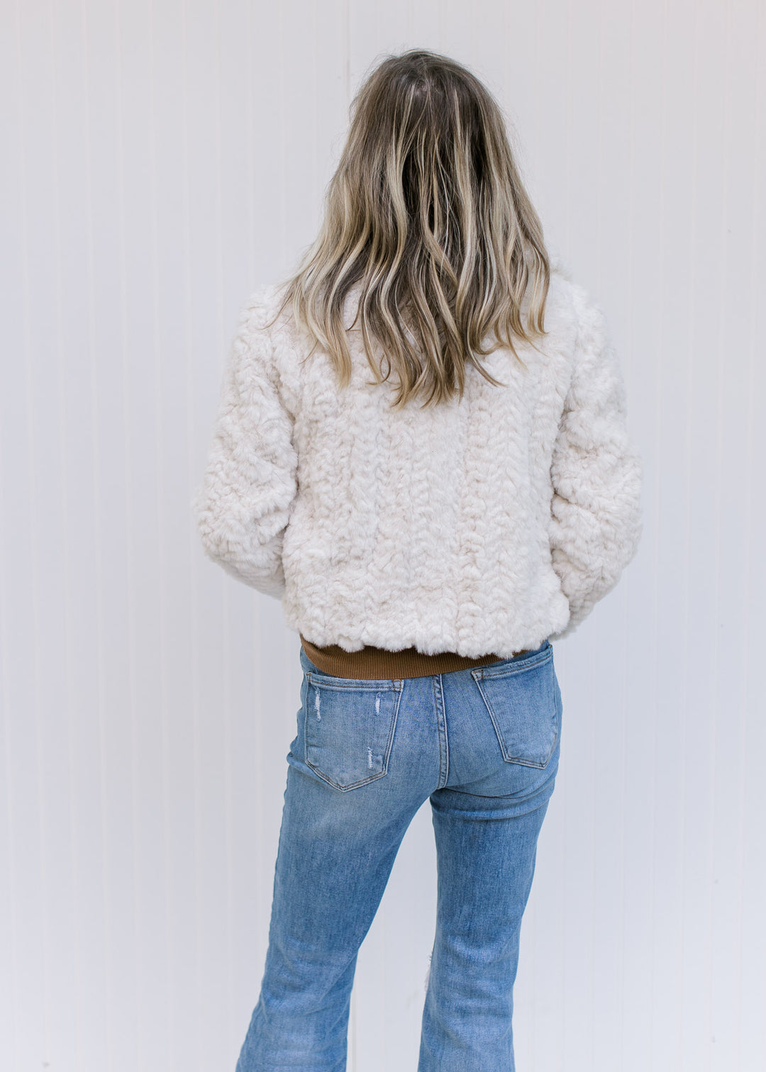 Back view of Model wearing an ivory open front coat with a crop cut, pockets and long sleeves. 