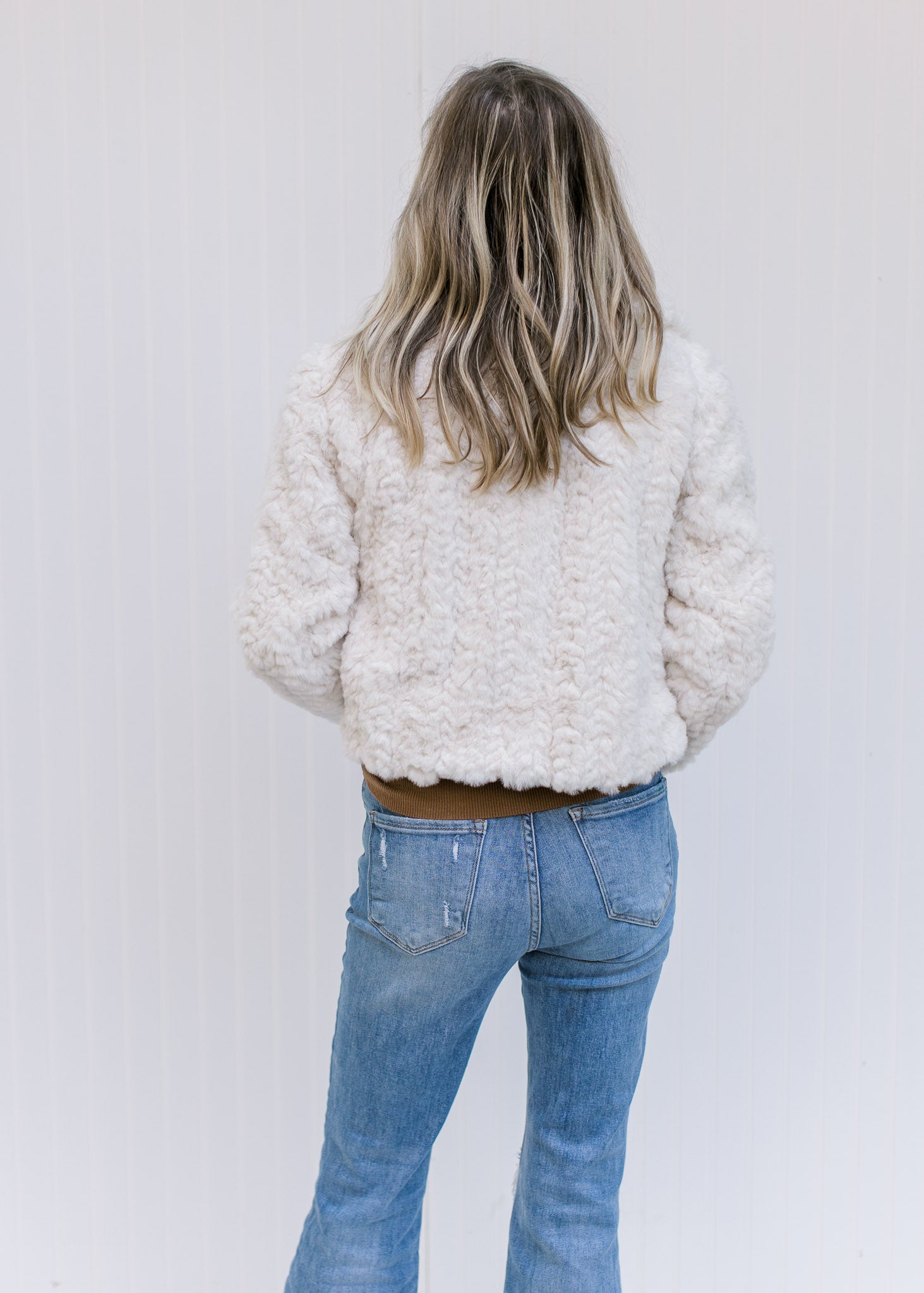 Back view of Model wearing an ivory open front coat with a crop cut, pockets and long sleeves. 