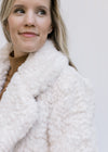 Close up of collar on a Model wearing an ivory open front coat with a crop cut and long sleeves. 