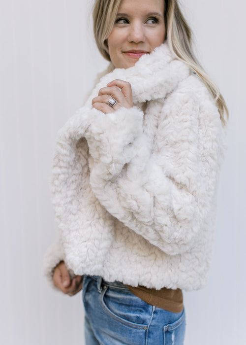 Model wearing an ivory open front coat with a crop cut, pockets and long sleeves. 