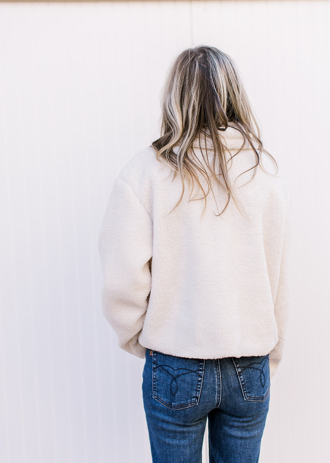 Back view of model wearing a fuzzy cream jacket with faux leather strap and patch pockets.