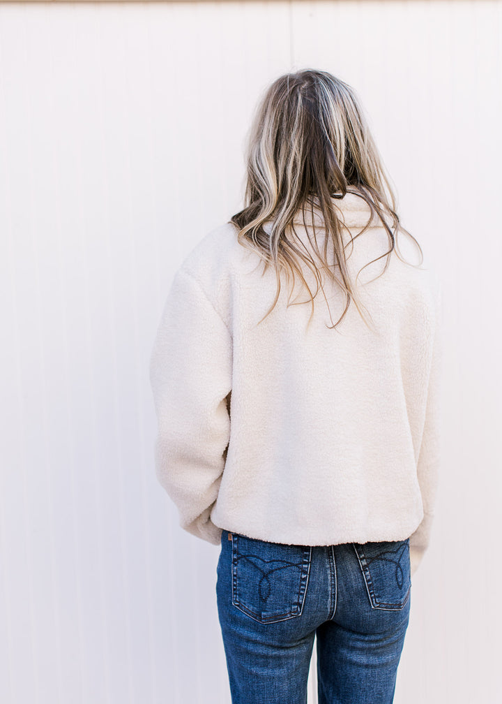 Back view of model wearing a fuzzy cream jacket with faux leather strap and patch pockets.