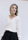 Model wearing a cream long sleeve top with pearl embellishments at v-neck and a fuzzy finish. 