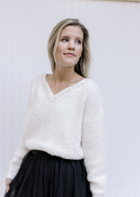 Model wearing a cream long sleeve top with pearl embellishments at v-neck and a fuzzy finish. 