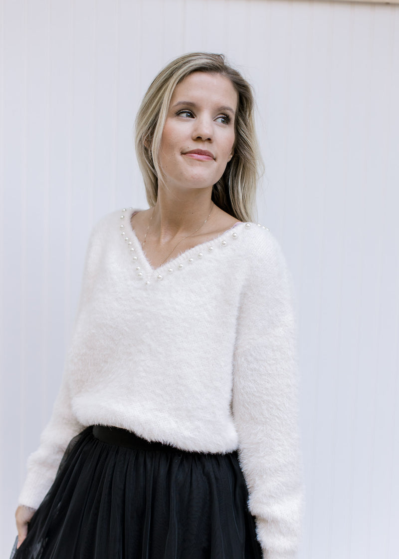 Model wearing a cream long sleeve top with pearl embellishments at v-neck and a fuzzy finish. 