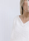 Close up of pearl embellishments at v-neck on a fuzzy cream long sleeves sweater. 