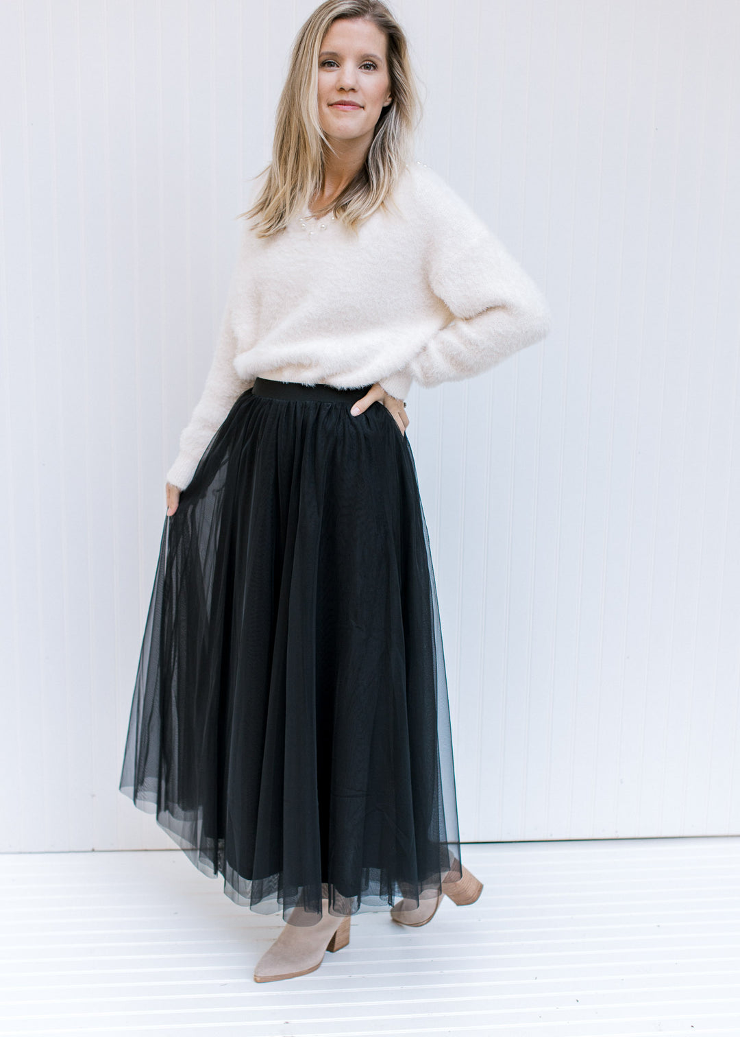 Model wearing a black maxi with a cream long sleeve sweater with pearl embellishments at v-neck. 