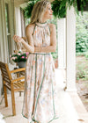 Model wearing a pale pink dress with a blue, pink, green and gray floral design and a halter fit.