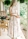 Model wearing a pale pink midi with a floral design, green piping, a halter fit and elastic waist.