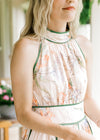 Close up of green piping ad halter neck on a sleeveless pale pink dress with a floral design. 