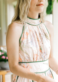 Close up of green piping ad halter neck on a sleeveless pale pink dress with a floral design. 
